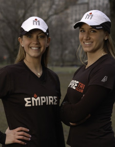 Two women wearing Empire sports attire outdoors.
