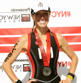 A woman standing in front of a red wall with medals around her neck.