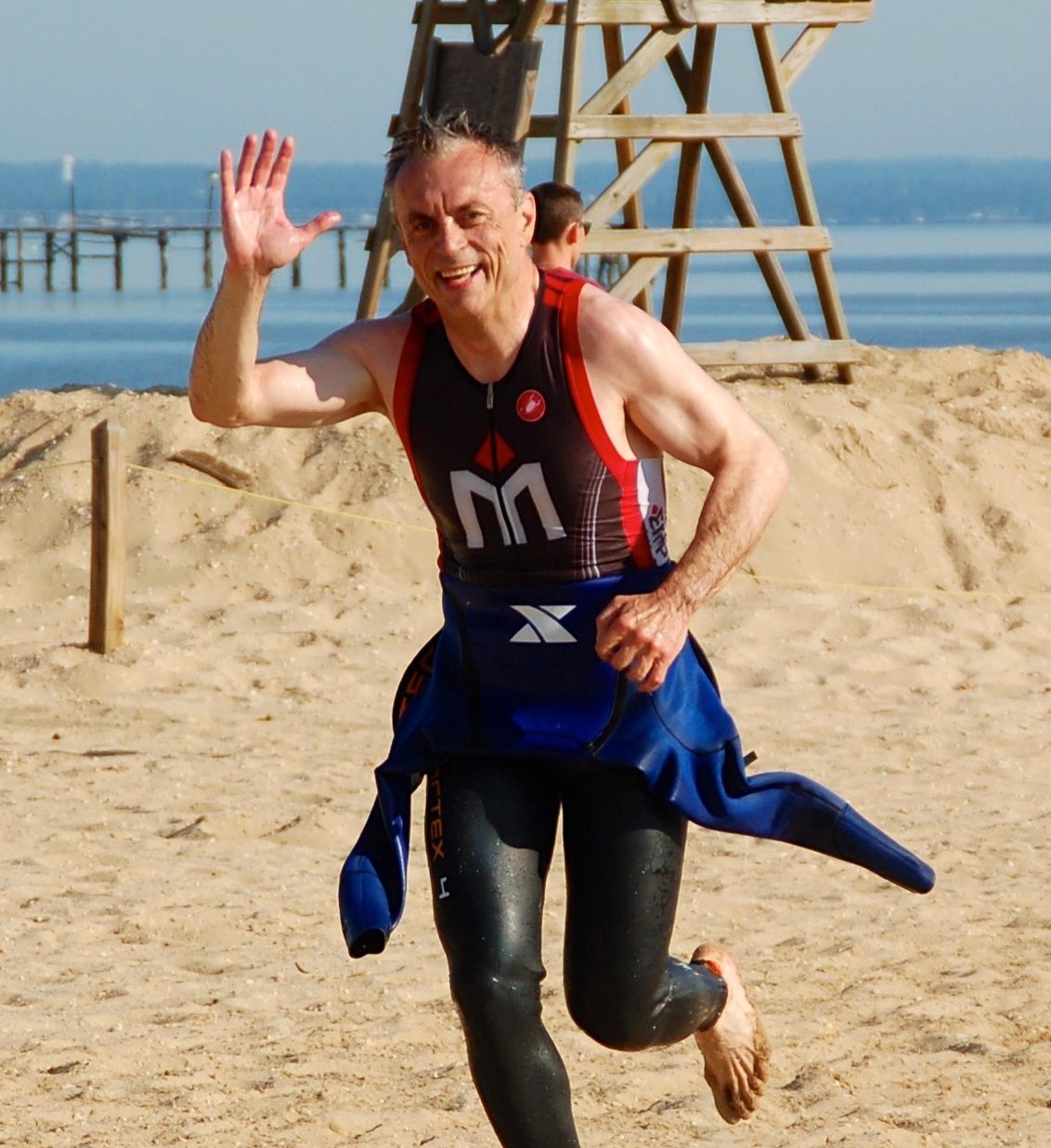 A man running on the beach in his wetsuit.