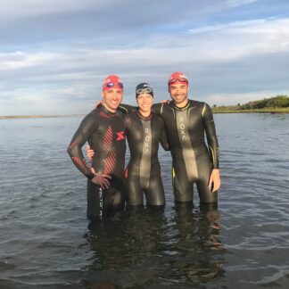 Three people in wet suits standing in the water.