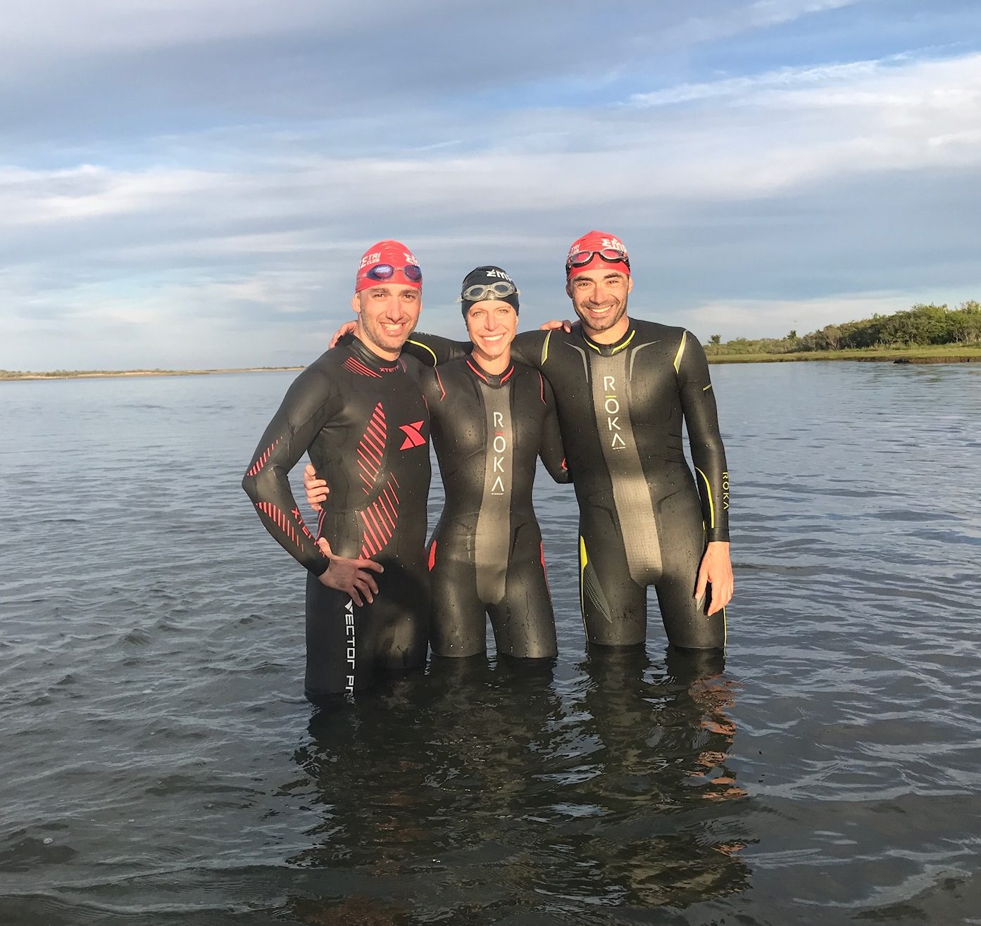 Three people in wet suits standing in the water.
