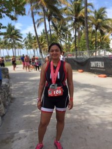 Runner with medals standing outdoors under palm trees.