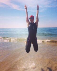 Person jumping joyfully in wetsuit at beach.