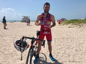 Cyclist on beach holding medals, near bike.