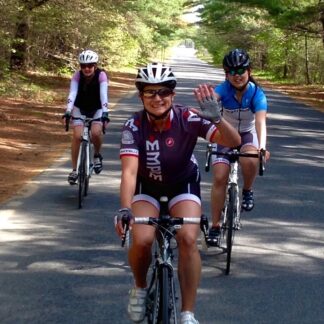 Three people riding bikes down a road with trees.
