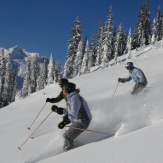 Two people skiing down a hill on the side of a mountain.