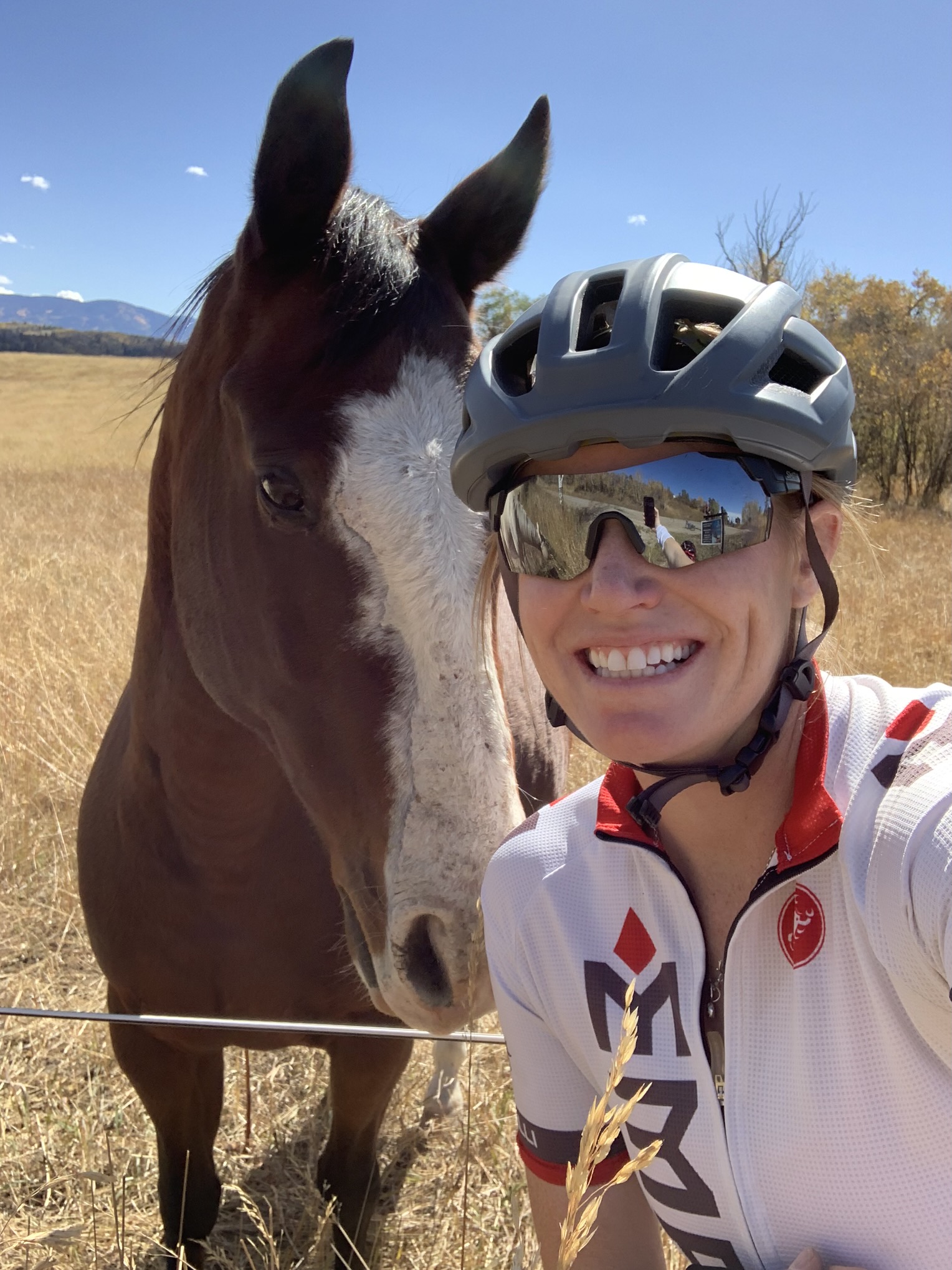 A woman in white jacket standing next to brown horse.