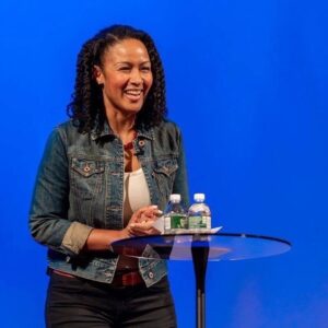 Smiling woman speaking, blue background, table.