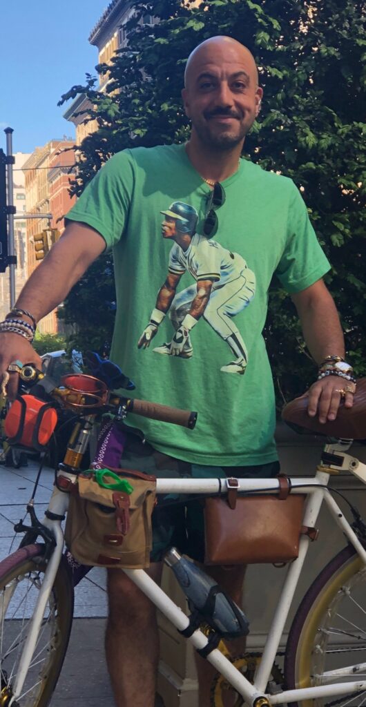Man with bicycle wearing green baseball shirt.