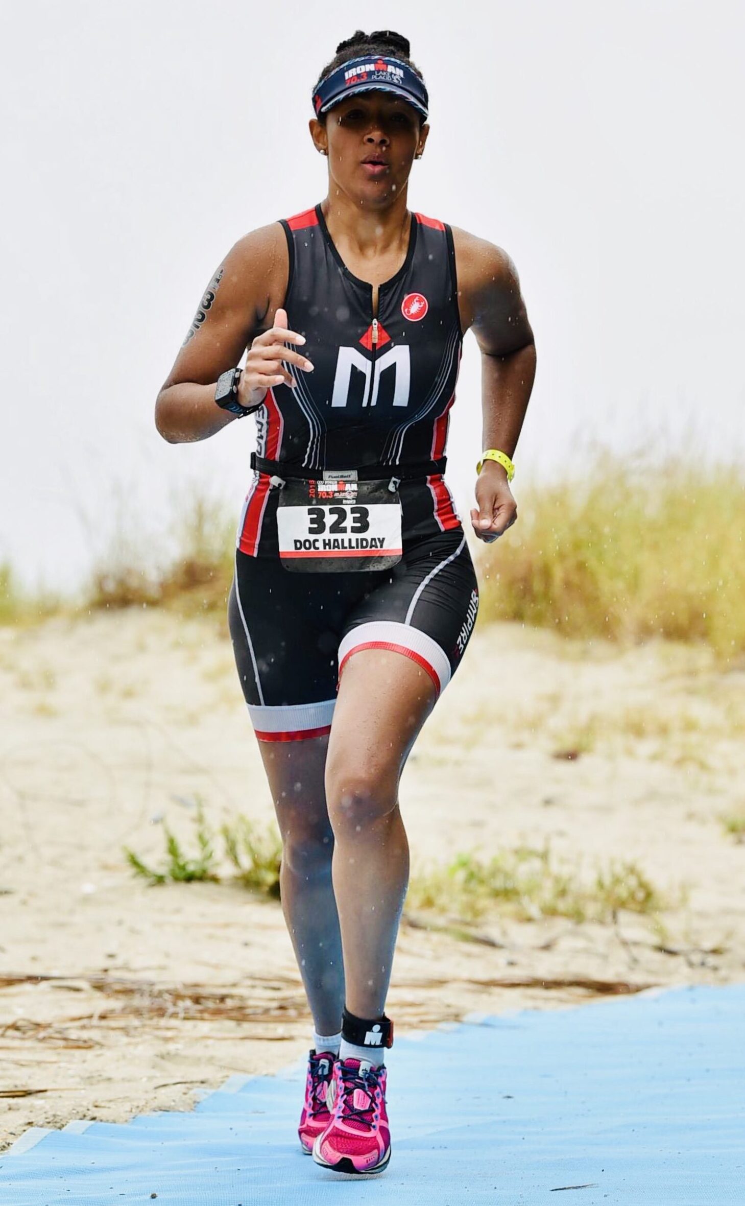 A man running on the beach wearing a race number.