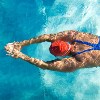 A man swimming in the water wearing a red hat.
