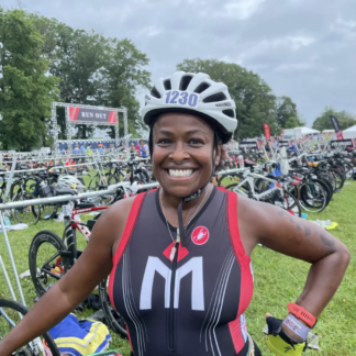 A woman in a triathlon gear standing next to many bikes.