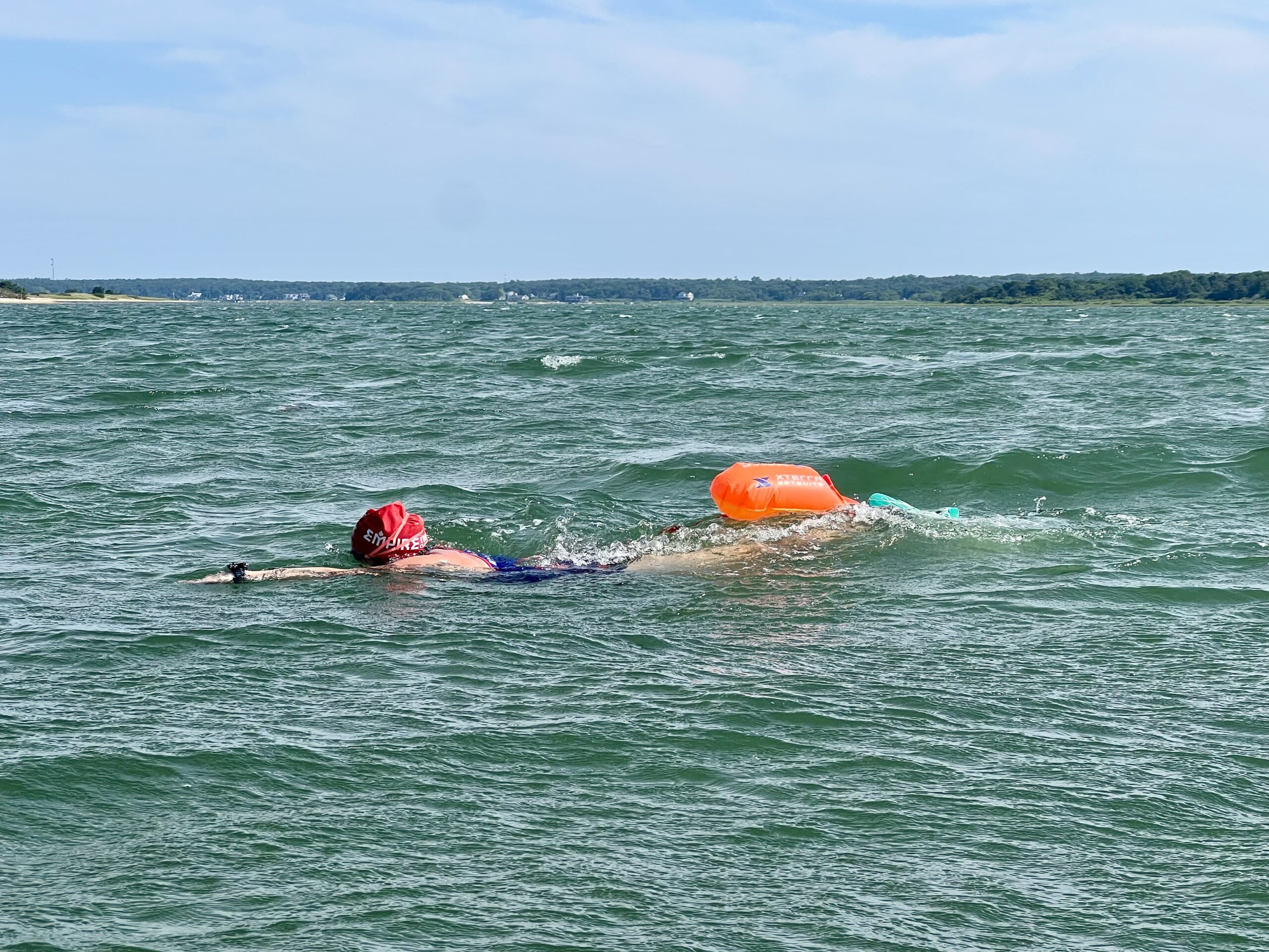 A person swimming in the ocean with an orange buoy.